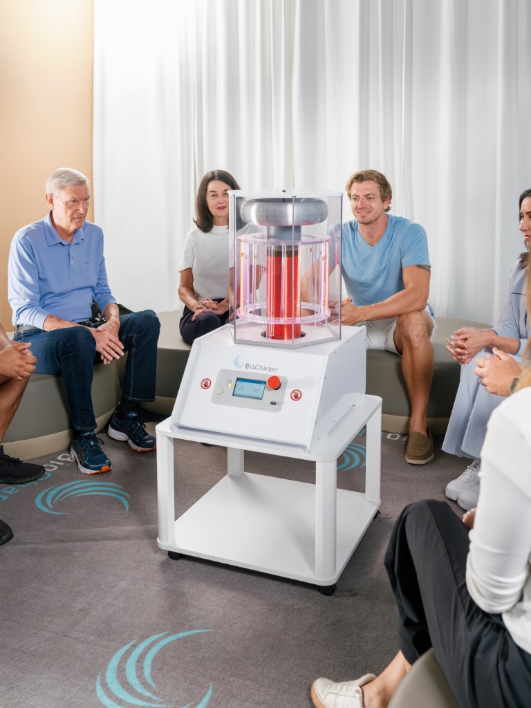 Group of people seated in a circle around a BioCharger energy device in a bright room.
